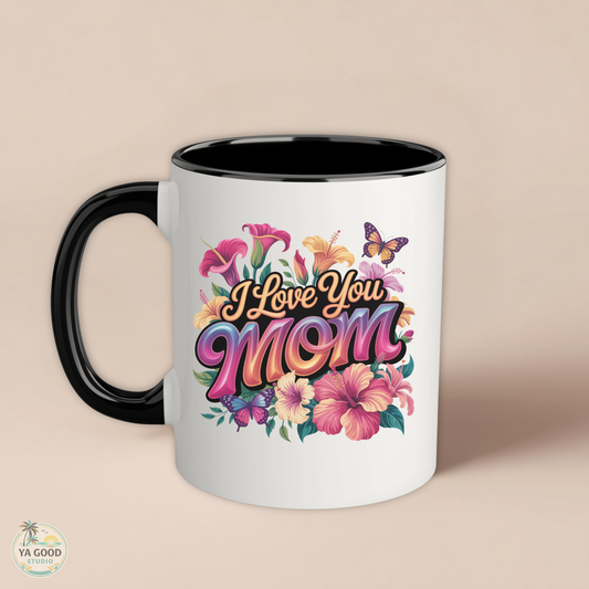 white mug with black trim that says "I Love you Mom" in floral pattern on beige background