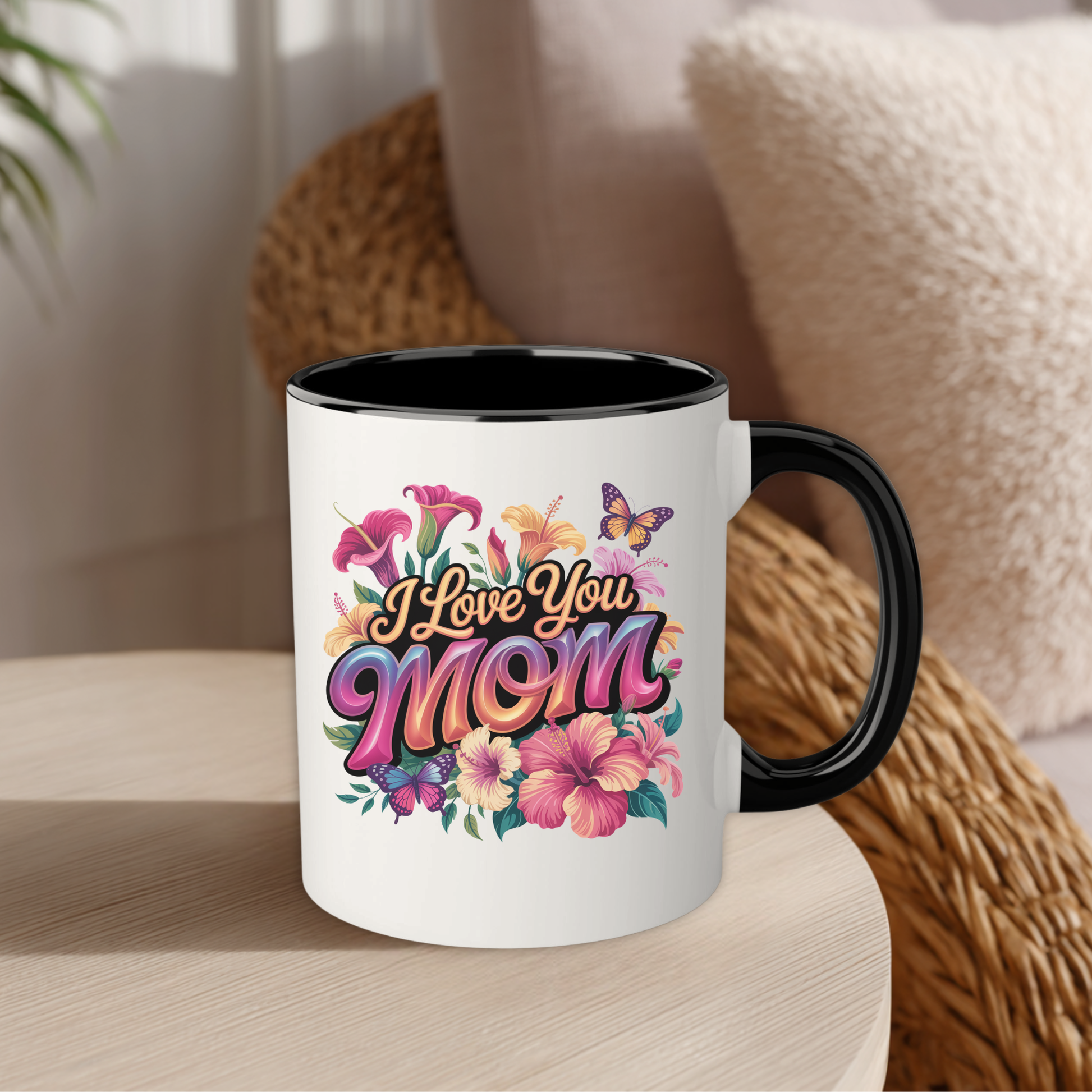 white mug with black trim that says "I Love you Mom" in floral pattern on a table on a blurred background