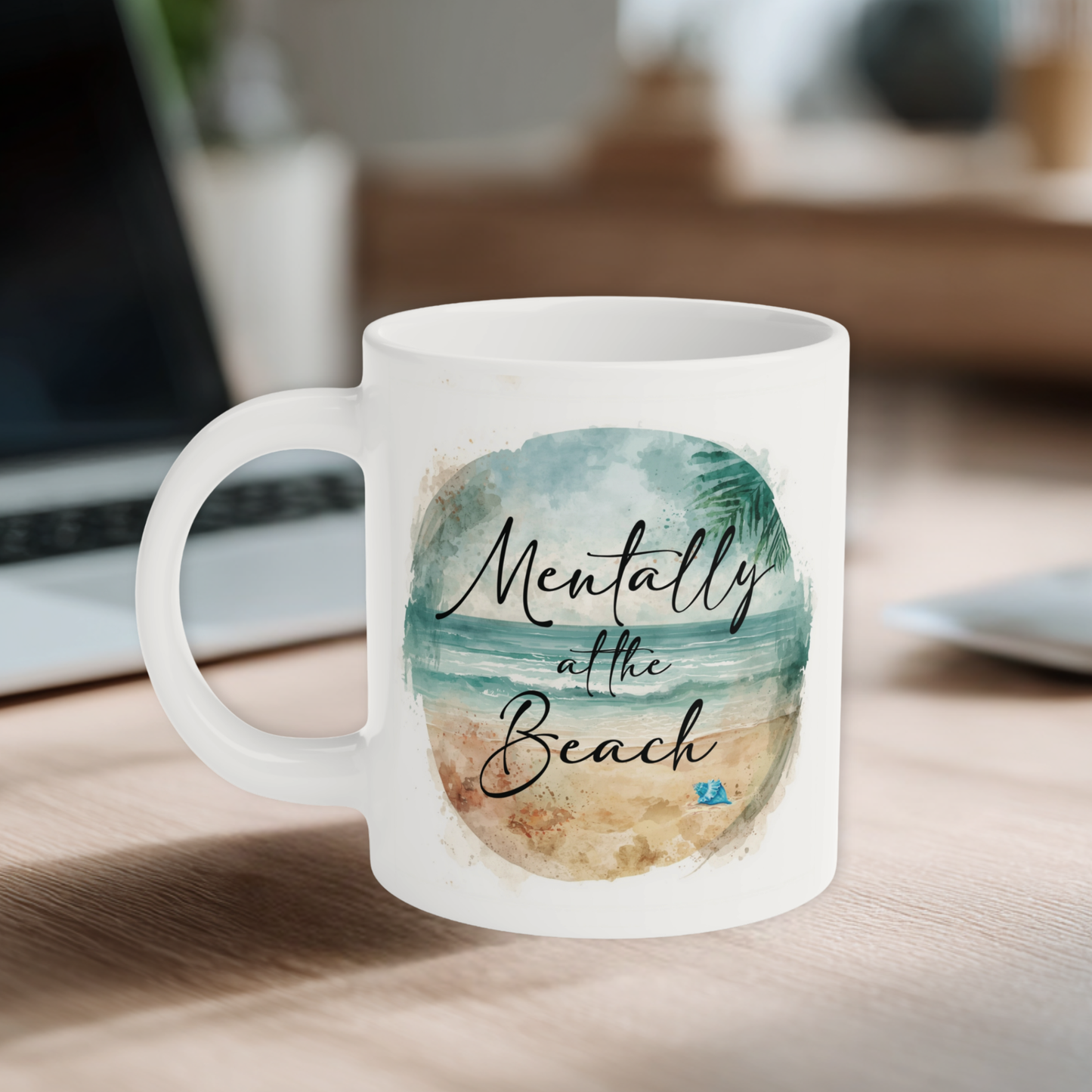 Mug with beach-themed design and text on a desk with a laptop in the background